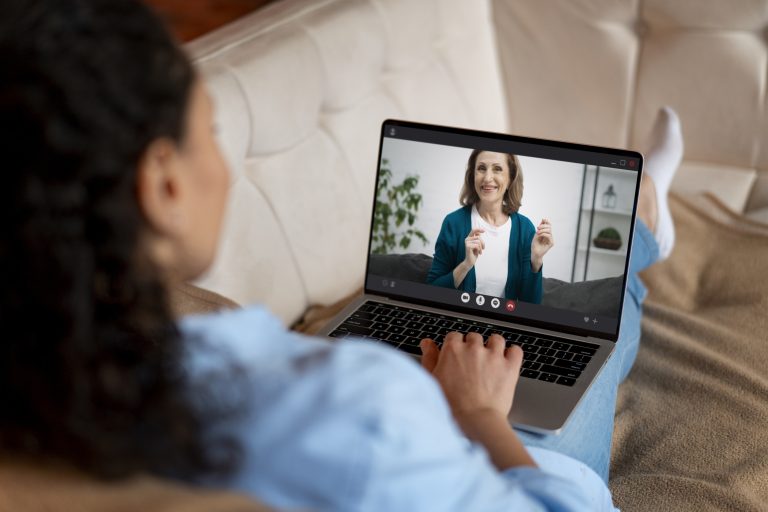 obieta prowadząca rozmowę wideo z uśmiechniętą terapeutką lub nauczycielką, siedzącą na kanapie. Spotkanie odbywa się online na ekranie laptopa.